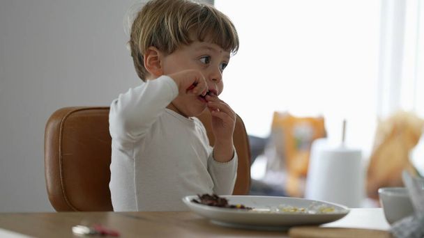 Toddler eating food by himself during lunch time baby using utensil - Zdjęcie, obraz