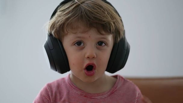 Pikkulapsi poika käyttää kuulokkeita yrittää laittaa, mutta sitten poistaa kuulokkeet - Valokuva, kuva