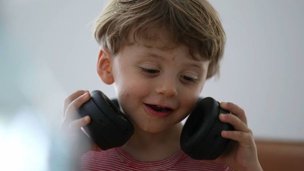 Pikkulapsi poika käyttää kuulokkeita yrittää laittaa, mutta sitten poistaa kuulokkeet - Valokuva, kuva
