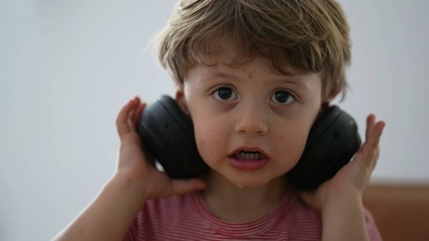 Kleinkind Junge mit Kopfhörern versucht, setzen, aber dann entfernen Kopfhörer - Foto, Bild