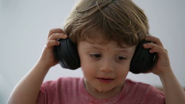 Tout-petit garçon en utilisant des écouteurs essayant de mettre, mais puis enlever les écouteurs - Photo, image