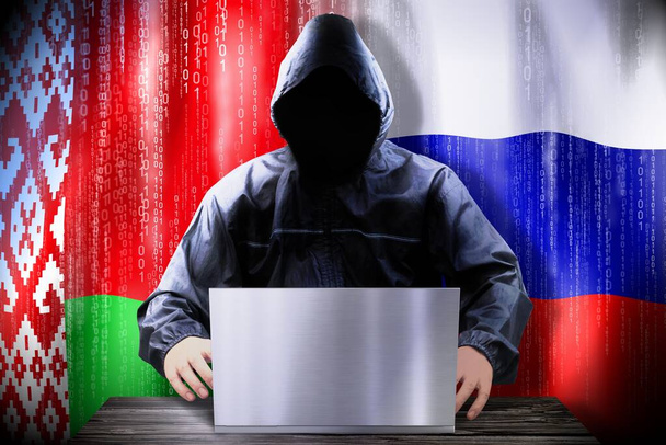 Ανώνυμος χάκερ που δουλεύει σε λάπτοπ, σημαίες Λευκορωσίας και Ρωσίας. - Φωτογραφία, εικόνα