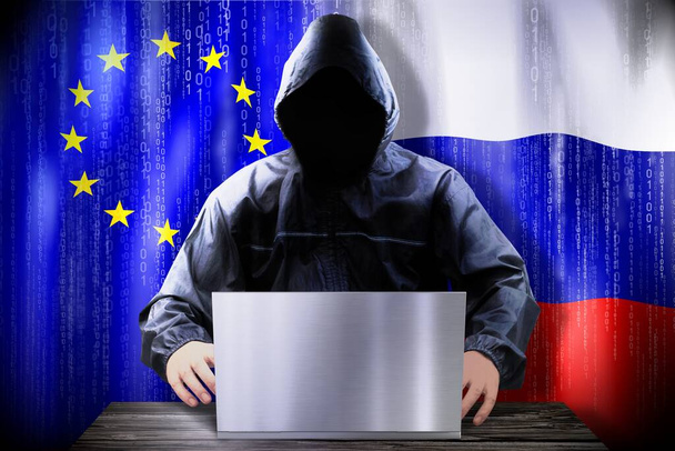 Pirate anonyme travaillant sur un ordinateur portable, drapeaux de l'Union européenne et la Russie - Photo, image