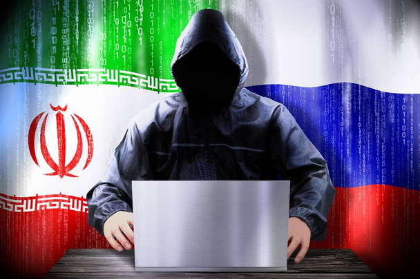 Anonymous hacker working on a laptop, flags of Iran and Russia - Photo, Image