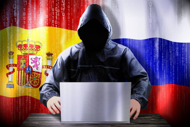 Anonyme Hacker arbeiten an einem Laptop, Flaggen Spaniens und Russlands - Foto, Bild