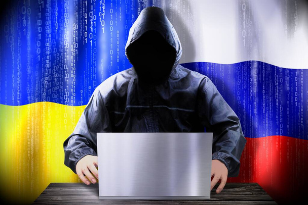 Anonyme Hacker arbeiten an einem Laptop, Flaggen der Ukraine und Russlands - Foto, Bild