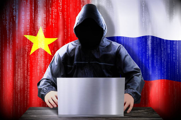 hacker anónimo trabajando en una computadora portátil, banderas de Vietnam y Rusia - Foto, Imagen