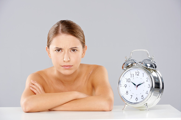 Mujer con brazos cruzados al lado del reloj despertador
 - Foto, Imagen