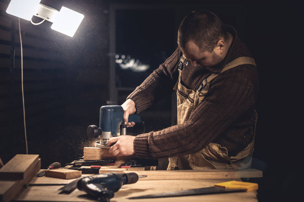 Um homem faz produtos de madeira com a ajuda de ferramentas especiais. Retrato de um jovem carpinteiro no trabalho. Emprego na indústria madeireira - Foto, Imagem