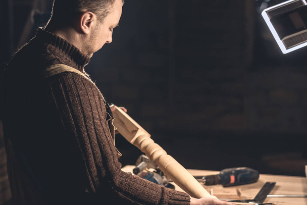 Ein Mann stellt mit Hilfe spezieller Werkzeuge Holzprodukte her. Porträt eines jungen Zimmermanns bei der Arbeit. Beschäftigung in der holzbearbeitenden Industrie - Foto, Bild