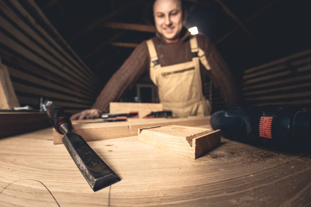 Un hombre hace productos de madera con la ayuda de herramientas especiales. Retrato de un joven carpintero en el trabajo. Empleo en la industria maderera - Foto, Imagen