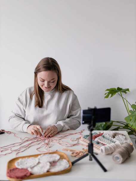 Woman record new videovlog in living room. Puts smartphone on tripod girl make online live stream, lead webinar distant chat, modern tech, video concept. Handmade macrame in work process. Female hobby - Foto, afbeelding