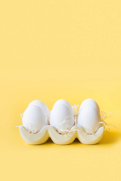 Organic white chicken eggs in porcelain decorative box on yellow. - Foto, afbeelding