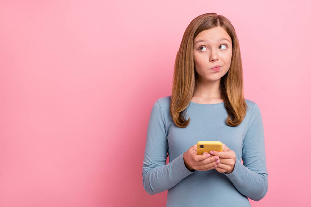 Portrait of attractive minded unsure girl using gadget deciding copy blank space isolated over pink pastel color background - Fotografie, Obrázek