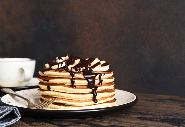 Stack of pancakes with banana and chocolate sauce on wooden brown background - Foto, Imagem