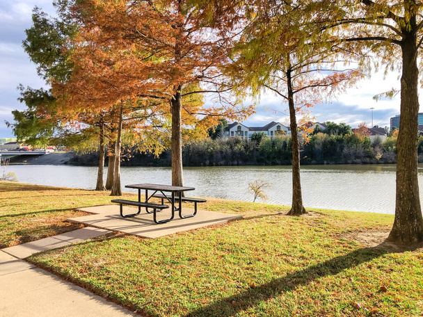 Стол для пикника под лысым кипарисом с видом на задний двор жилого комплекса на берегу реки в Ирвинге, штат Техас, Америка. Аренда жилья на набережной общины с осенней листвы, чистый бетонный путь - Фото, изображение
