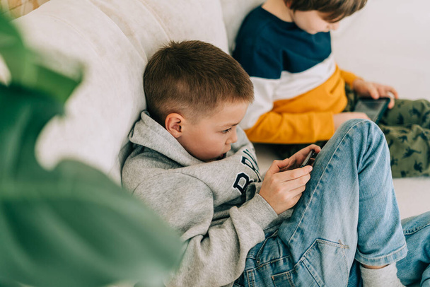 Vidám két Childs fiúk online játék, videó nézés mobilon. Mosolygó gyerekek vicces mobil alkalmazásokat használnak, élvezik az otthon töltött szabadidőt a kanapén. A testvérek együtt játszanak a telefonban. - Fotó, kép