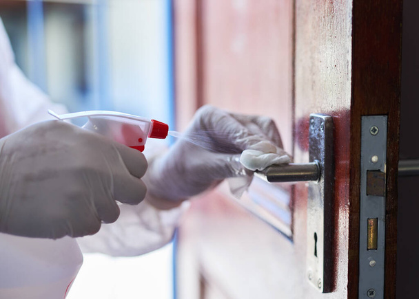 Um profissional de limpeza pulveriza desinfetante em uma maçaneta da porta - Foto, Imagem