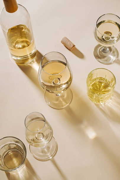 Vino bianco servito in bicchieri di cristallo assortiti visti dall'alto verso il basso con ombra su uno sfondo beige con spazio copia per feste o feste - Foto, immagini