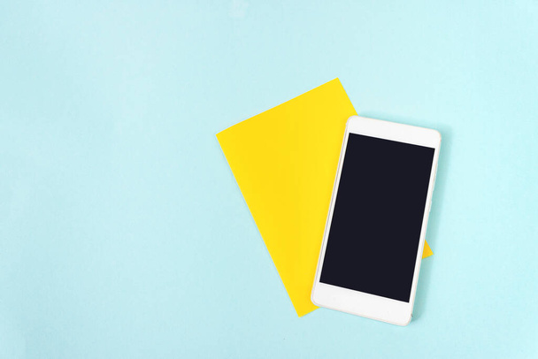 Amarillo un pedazo de papel con pantalla vacía teléfono móvil sobre fondo azul - Foto, imagen