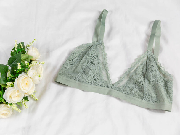 Sexy Damenunterwäsche und Blumen auf dem Bett. Grüner BH, Spitzenwäsche auf weißem Bettlaken. Beauty-Blogger-Konzept. Draufsicht, flache Lage - Foto, Bild