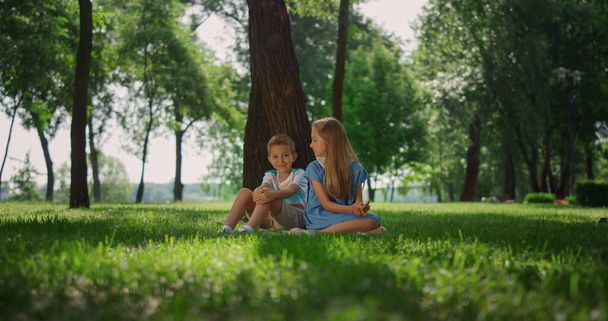 Šťastné děti sedí u stromu na zelené trávě. Roztomilý chlapec dívka hrát na přírodu. - Fotografie, Obrázek