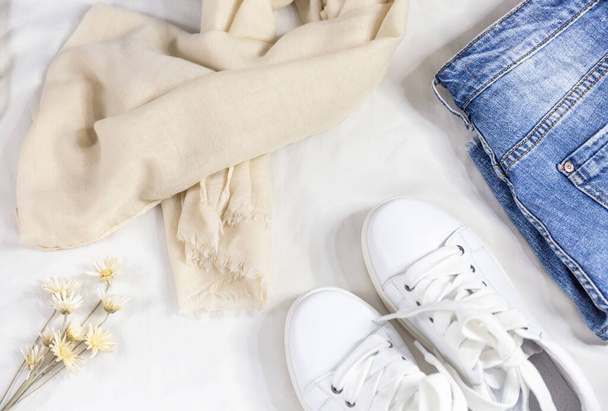 Echarpe en jean bleu, sac et baskets blanches sur lit blanc. Tenue d'été ou de printemps élégante pour femmes. Des vêtements à la mode. Couché plat, vue du dessus. - Photo, image