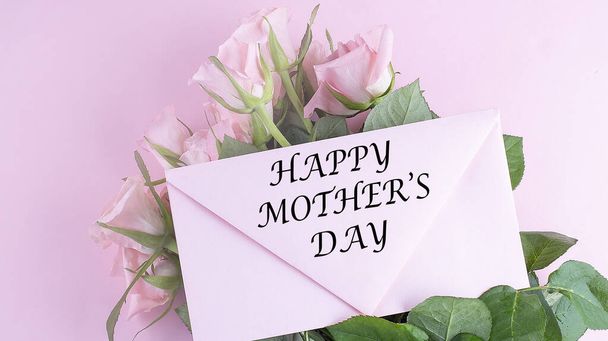 Detailní záběr krásné kytice růží se šťastným textem dne matek na růžové obálce. Koncept Den matek - Fotografie, Obrázek