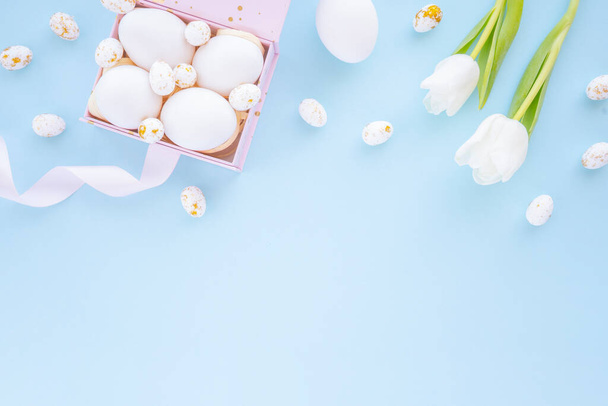 Widok z góry kolorowych jaj w pudełku z tulipanami, na wiosenne wakacje Wielkanoc. Płaskie, niebieskie tło - Zdjęcie, obraz