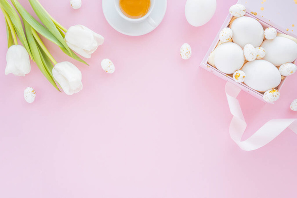 Top view of colorful eggs in a box with tulips, cup of tea for spring holiday easter. Flat lay, pink background - 写真・画像