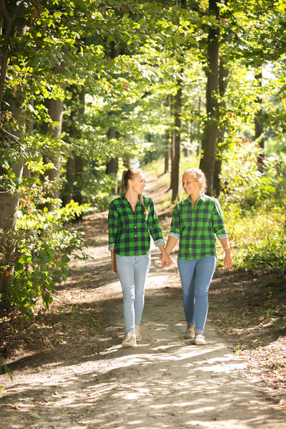 Girls in shirts and jeans walking in forest at sunny day - Fotoğraf, Görsel