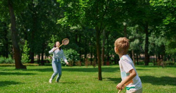 Active boy playing badminton with mother back view. Sport in family life concept - Foto, afbeelding