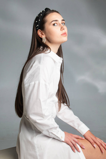 Sitting young woman with dark hair in white long sleeve blouse isolated on grey - Fotoğraf, Görsel