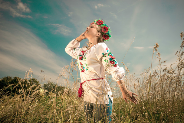 mooie vrouw in Oekraïense kleren bij veld op winderige dag - Foto, afbeelding