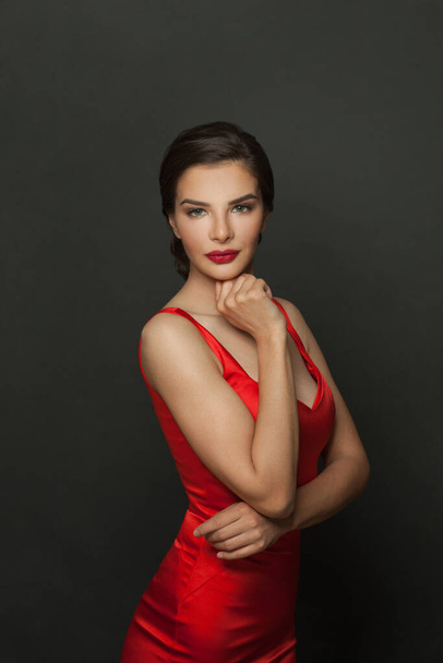 Atractiva mujer modelo de moda con maquillaje usando vestido rojo sedoso posando sobre fondo negro - Foto, imagen