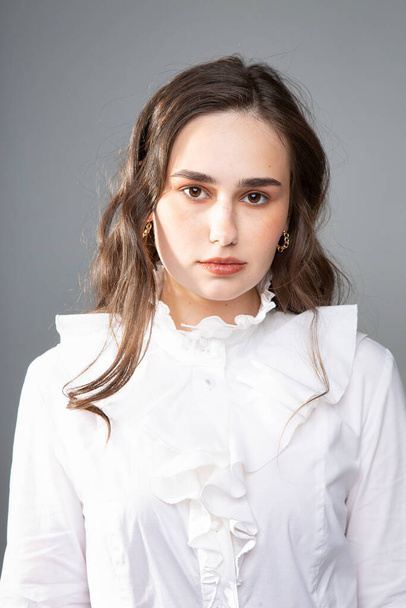 Portrait of young woman with long hair with dark brown eyes isolated on grey in white outfit - Foto, Imagen