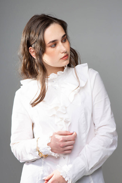 Looking away young woman with long hair with dark brown eyes isolated on grey in white outfit - Fotó, kép