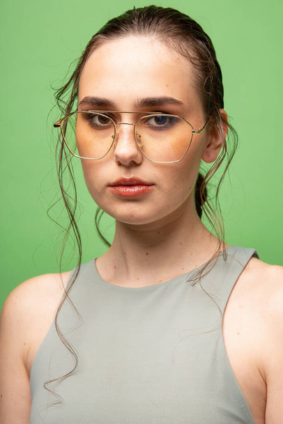 Portrait of young woman with gathered dark hair in glasses isolated on green - Foto, afbeelding