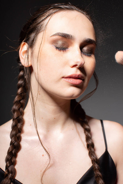 Portrait of making makeup young european woman with two braids with closed eyes isolated on dark grey - Photo, image