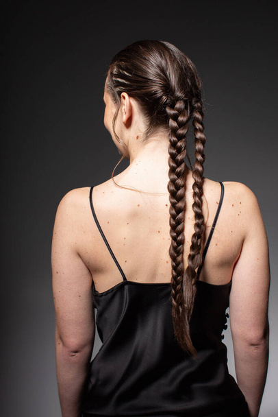 Turned back young european woman with two braids isolated on dark grey in total black outfit - Zdjęcie, obraz