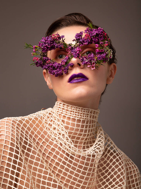 Woman with eye mask made of small flowers with purple lips portrait isolated on grey brown - Foto, Imagen