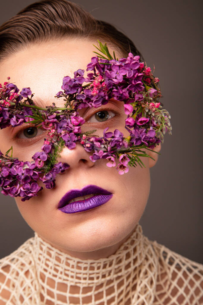 Woman with eye mask made of small flowers with purple lips portrait isolated on grey brown - Foto, imagen