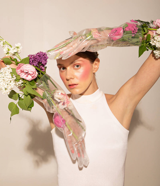 Europejka z zebranymi włosami z jasnoróżowymi rumieńcami i pastelowymi kwiatami przyczepionymi do rąk odizolowanych na beżu - Zdjęcie, obraz