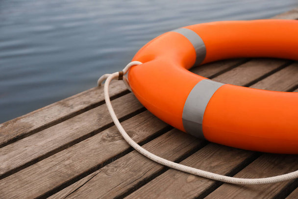 Orange lifebuoy on wooden pier near water. Rescue equipment - Fotó, kép