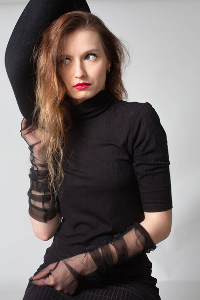 White young european woman in total black isolated on grey with red lips - Foto, afbeelding