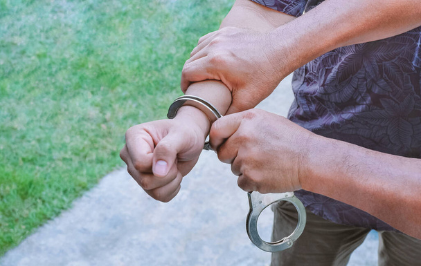 Close up burger politie handen handboeien jonge schurk man met wazig outdoor achtergrond - Foto, afbeelding