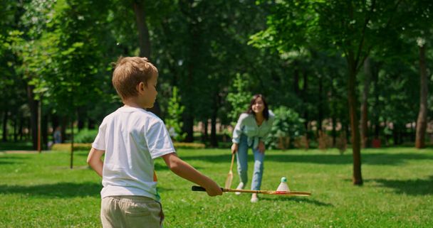 Vreugdevolle moeder speelt badminton met zoon in park. Gelukkig gezin veel plezier buiten. - Foto, afbeelding