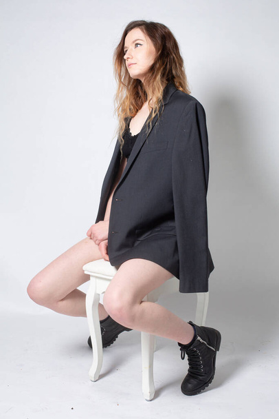 White young european woman sitting on the chair isolated on light grey in total black - Photo, Image
