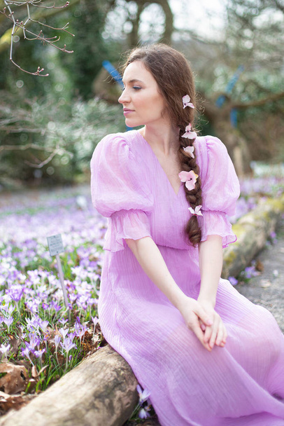 European woman with long hair in lilac dress sitting with pigtail in park - Photo, Image