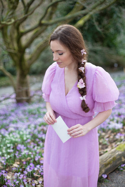 European woman in lilac dress with brown hair standing in park - Fotoğraf, Görsel